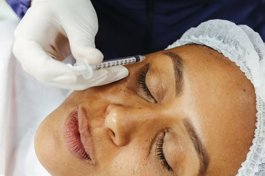 Gloved hand giving a facial injection to a client lying with her eyes closed