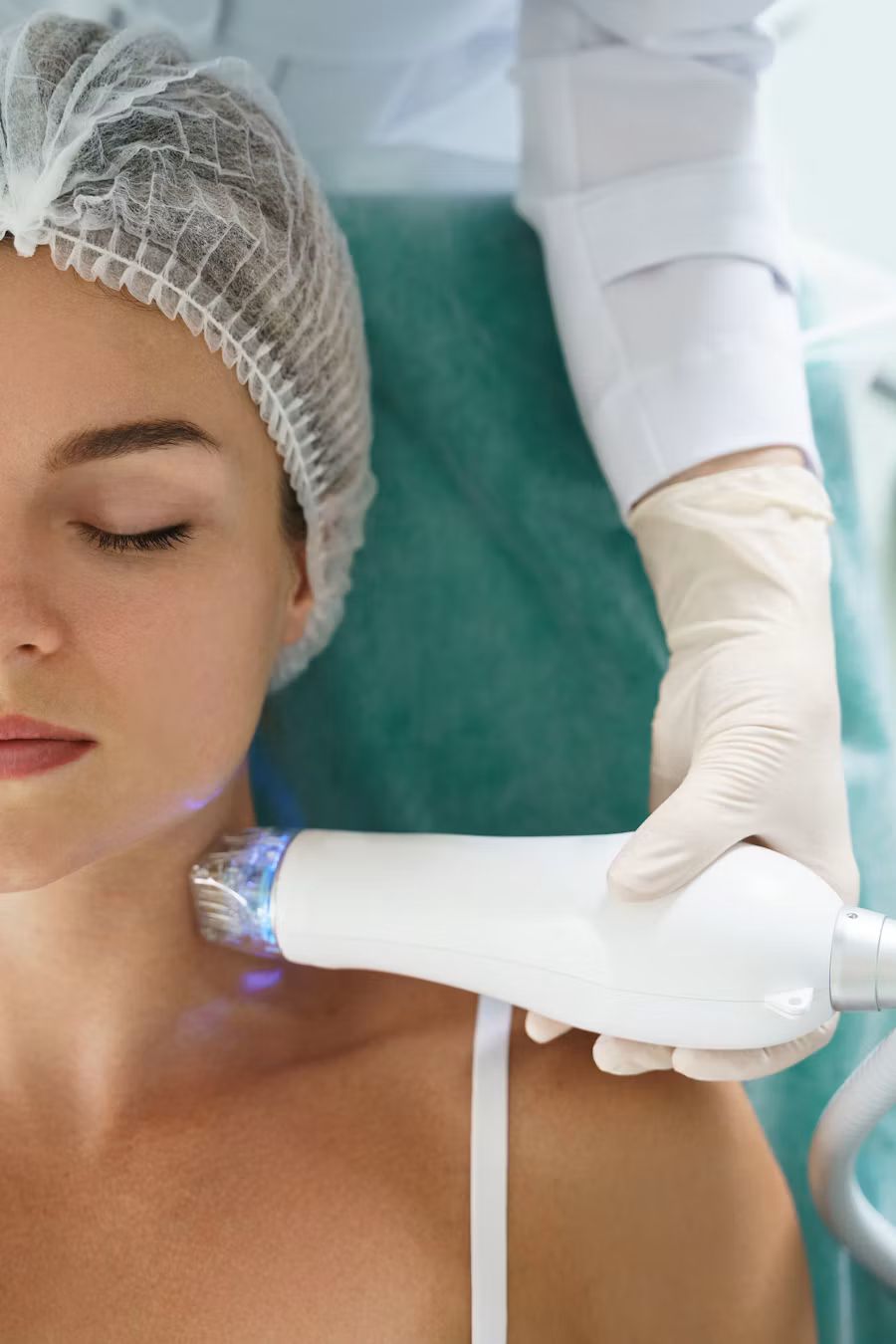 Clinician in gloves using a handheld skin treatment device on a client's neck